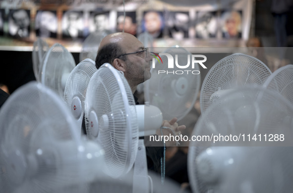 An Iranian man is praying while standing between fans that are cooling a mosque, during a religious festival to commemorate Tasoua, a day ah...