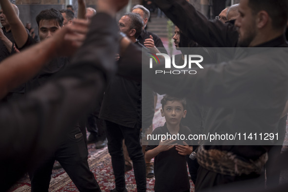 A young Iranian boy is looking at men who are beating themselves during a religious festival to commemorate Tasoua, a day ahead of Ashura, a...