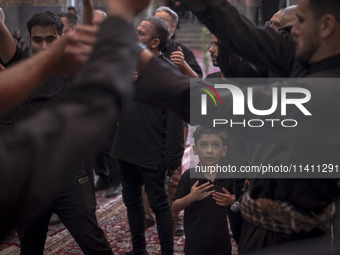 A young Iranian boy is looking at men who are beating themselves during a religious festival to commemorate Tasoua, a day ahead of Ashura, a...