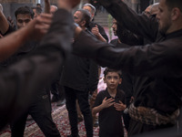 A young Iranian boy is looking at men who are beating themselves during a religious festival to commemorate Tasoua, a day ahead of Ashura, a...