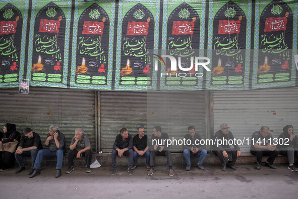 Iranian people are sitting under a religious banner during a religious festival to commemorate Tasoua, a day ahead of Ashura, in the Grand B...