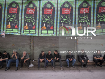 Iranian people are sitting under a religious banner during a religious festival to commemorate Tasoua, a day ahead of Ashura, in the Grand B...