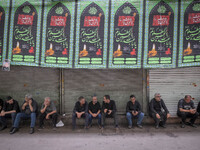 Iranian people are sitting under a religious banner during a religious festival to commemorate Tasoua, a day ahead of Ashura, in the Grand B...