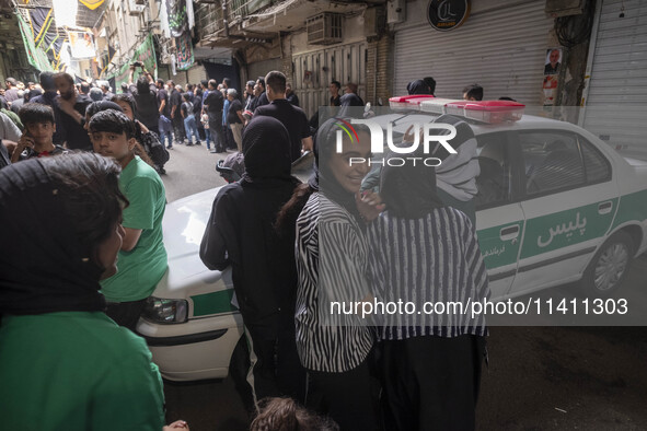 A young Iranian woman is smiling while standing next to a police vehicle with her relatives, during a religious festival to commemorate Taso...