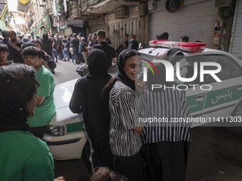 A young Iranian woman is smiling while standing next to a police vehicle with her relatives, during a religious festival to commemorate Taso...