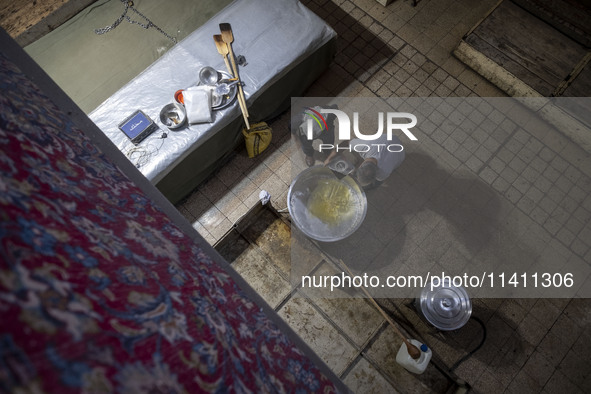 An Iranian man is loading oil into a large pot to bake donated meals during a religious festival to commemorate Tasoua, a day ahead of Ashur...