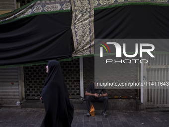 A young Iranian man is using his cellphone while sitting under a giant religious flag at a bazaar, before participating in a religious festi...