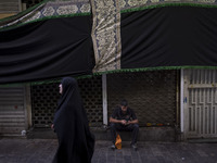 A young Iranian man is using his cellphone while sitting under a giant religious flag at a bazaar, before participating in a religious festi...