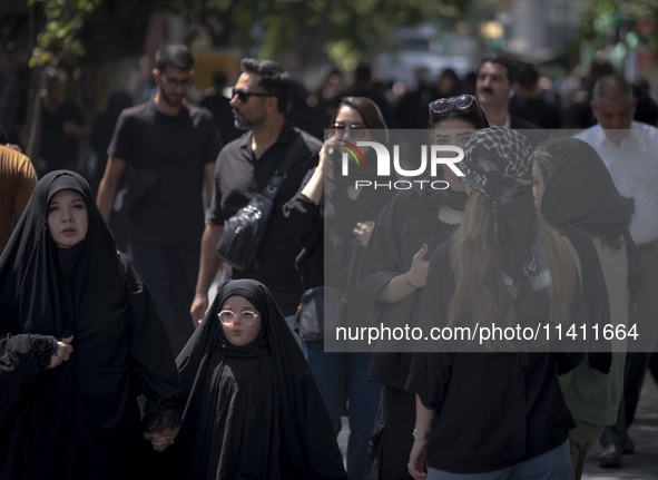 A veiled woman and her veiled daughter are walking past Iranian youths, out of the Grand Bazaar (Market), during a religious festival to com...