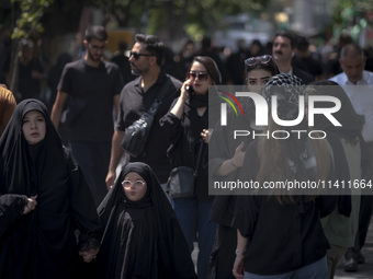 A veiled woman and her veiled daughter are walking past Iranian youths, out of the Grand Bazaar (Market), during a religious festival to com...