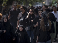 A veiled woman and her veiled daughter are walking past Iranian youths, out of the Grand Bazaar (Market), during a religious festival to com...