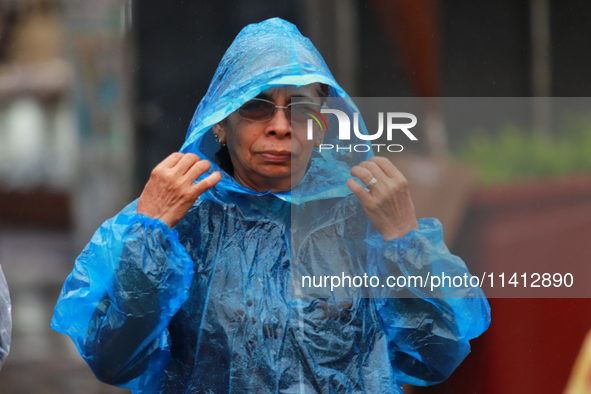 A person is covering herself from the rain with a raincoat while walking in downtown Mexico City, Mexico, on July 10, 2024. 