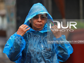 A person is covering herself from the rain with a raincoat while walking in downtown Mexico City, Mexico, on July 10, 2024. (