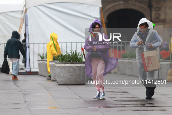 A person is covering herself from the rain with a raincoat while walking in downtown Mexico City, Mexico, on July 10, 2024. 