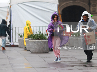 A person is covering herself from the rain with a raincoat while walking in downtown Mexico City, Mexico, on July 10, 2024. (