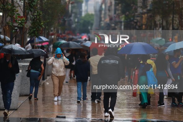 People are covering themselves from the rain with umbrellas while walking through downtown in Mexico City, Mexico, on July 10, 2024. 