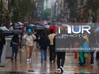 People are covering themselves from the rain with umbrellas while walking through downtown in Mexico City, Mexico, on July 10, 2024. (