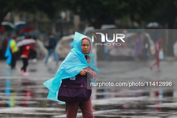 A person is covering herself from the rain with a raincoat while walking in downtown Mexico City, Mexico, on July 10, 2024. 