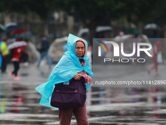 A person is covering herself from the rain with a raincoat while walking in downtown Mexico City, Mexico, on July 10, 2024. (