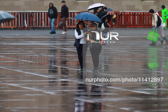 People are covering themselves from the rain with umbrellas while walking through downtown in Mexico City, Mexico, on July 10, 2024. 