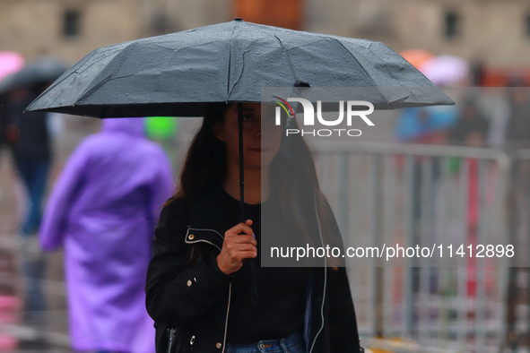 A person is covering herself from the rain with an umbrella while walking through downtown in Mexico City, Mexico, on July 10, 2024. 