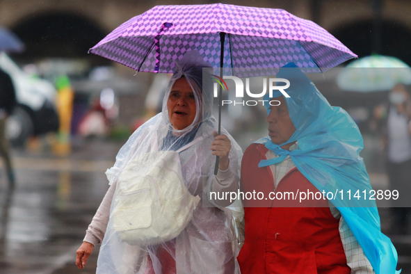 People are covering themselves from the rain with umbrellas while walking through downtown in Mexico City, Mexico, on July 10, 2024. 