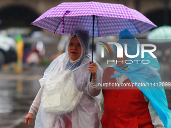 People are covering themselves from the rain with umbrellas while walking through downtown in Mexico City, Mexico, on July 10, 2024. (