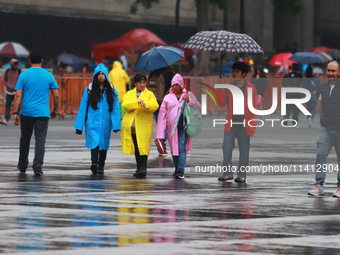 People are covering themselves from the rain with umbrellas while walking through downtown in Mexico City, Mexico, on July 10, 2024. (