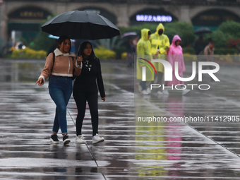 People are covering themselves from the rain with umbrellas while walking through downtown in Mexico City, Mexico, on July 10, 2024. (