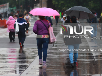 People are covering themselves from the rain with umbrellas while walking through downtown in Mexico City, Mexico, on July 10, 2024. (