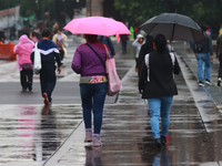 People are covering themselves from the rain with umbrellas while walking through downtown in Mexico City, Mexico, on July 10, 2024. (