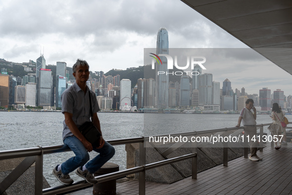 A man is sitting at the promenade in front of the Hong Kong Skyline in Hong Kong, on July 16, 2024. 