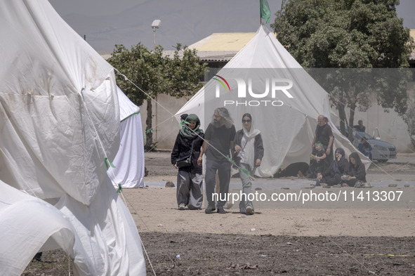 Youths are walking past the tents that are set up as symbols of the tents of Imam Hussein and his family, while participating in a religious...