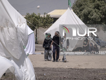 Youths are walking past the tents that are set up as symbols of the tents of Imam Hussein and his family, while participating in a religious...