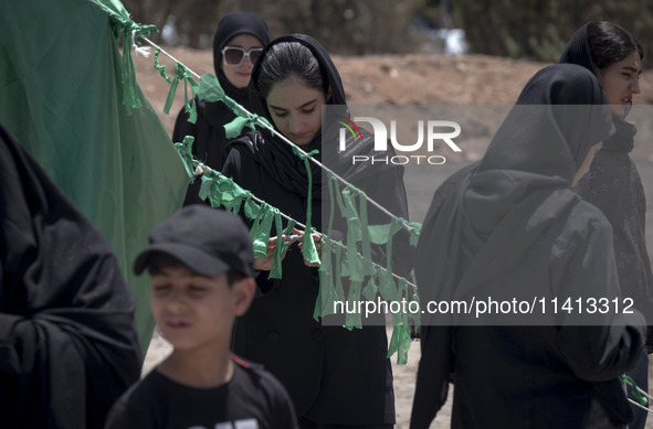 A young woman is tying a prayer symbol on a tent that is set up as a symbol of the tent of Imam Hussein during a religious festival to comme...