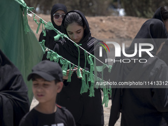 A young woman is tying a prayer symbol on a tent that is set up as a symbol of the tent of Imam Hussein during a religious festival to comme...