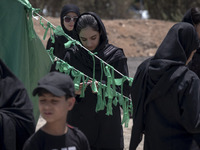 A young woman is tying a prayer symbol on a tent that is set up as a symbol of the tent of Imam Hussein during a religious festival to comme...