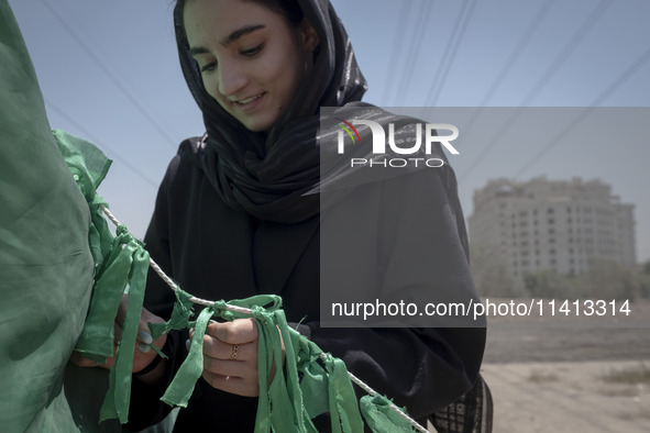 A young woman is tying a prayer symbol on a tent that is set up as a symbol of the tent of Imam Hussein during a religious festival to comme...