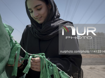 A young woman is tying a prayer symbol on a tent that is set up as a symbol of the tent of Imam Hussein during a religious festival to comme...