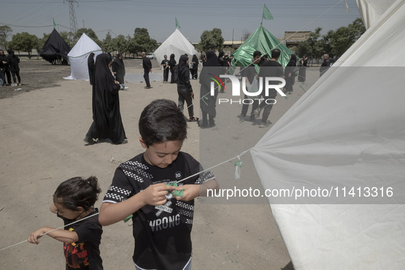 A young boy is tying a prayer symbol on a tent that is set up in an area, serving as a symbol of the tent of Imam Hussein's family, during a...