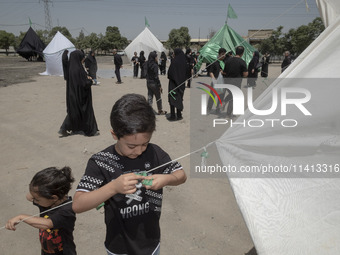 A young boy is tying a prayer symbol on a tent that is set up in an area, serving as a symbol of the tent of Imam Hussein's family, during a...