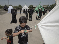 A young boy is tying a prayer symbol on a tent that is set up in an area, serving as a symbol of the tent of Imam Hussein's family, during a...