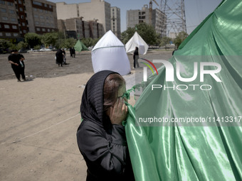 An Afghan refugee woman is praying while standing next to a tent that is set up as a symbol of the tent of Imam Hussein during a religious f...