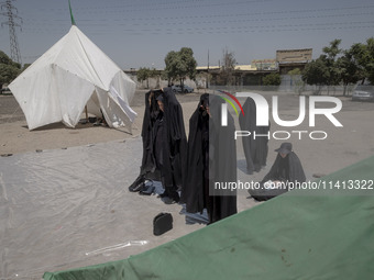 Veiled women are praying next to the tents that are set up in an area, serving as the symbol of the tents of Imam Hussein, during a religiou...