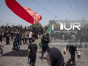 A young Iraqi boy living in Iran is waving a giant religious flag while participating in a religious festival to commemorate Ashura in the D...