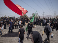 A young Iraqi boy living in Iran is waving a giant religious flag while participating in a religious festival to commemorate Ashura in the D...