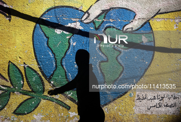 A Palestinian woman is walking past a mural painted on the wall of the UN school sheltering displaced people, following an Israeli strike, a...