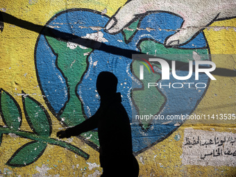 A Palestinian woman is walking past a mural painted on the wall of the UN school sheltering displaced people, following an Israeli strike, a...