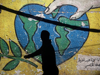 A Palestinian woman is walking past a mural painted on the wall of the UN school sheltering displaced people, following an Israeli strike, a...