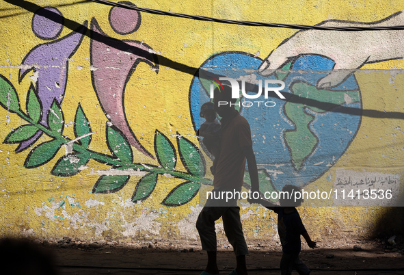 A man is walking with his children past a mural painted on the wall of the UN school sheltering displaced people, following an Israeli strik...